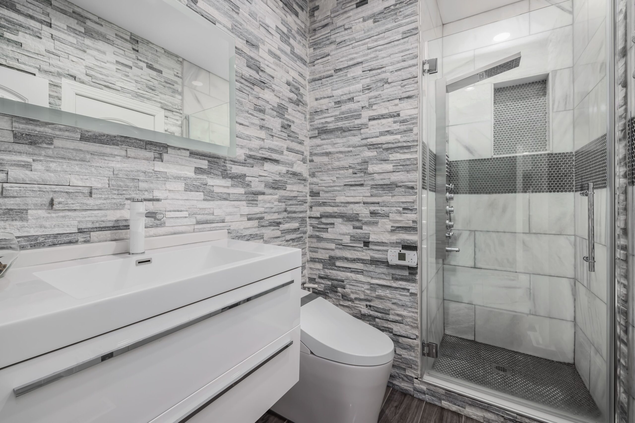 7 Bathroom Remodel Mistakes That Cost Evanston Homeowners Time and Money 1 Stylish modern bathroom featuring a glass shower, stone walls, and sleek white vanity.