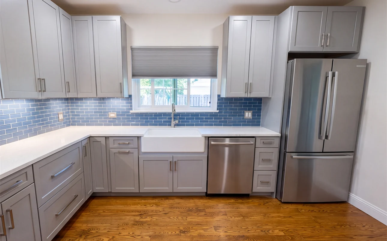 The finished sink wall with a full height blue glass subway tile backsplash, white apron front sink and under cabinet lighting