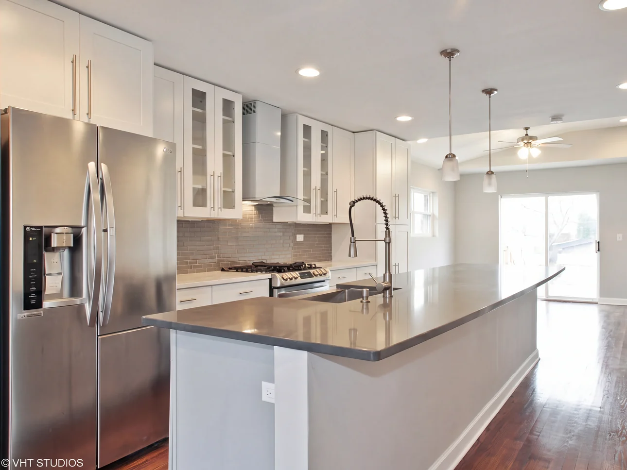 Kitchen remodel with a long quartz island, white cabinets and pendant lighting opening into the dining area